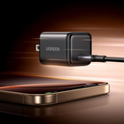 UGREEN black wall charger floating above a smartphone, with a charging cable extending from the side, set against a dark warm-toned background with motion blur effects.