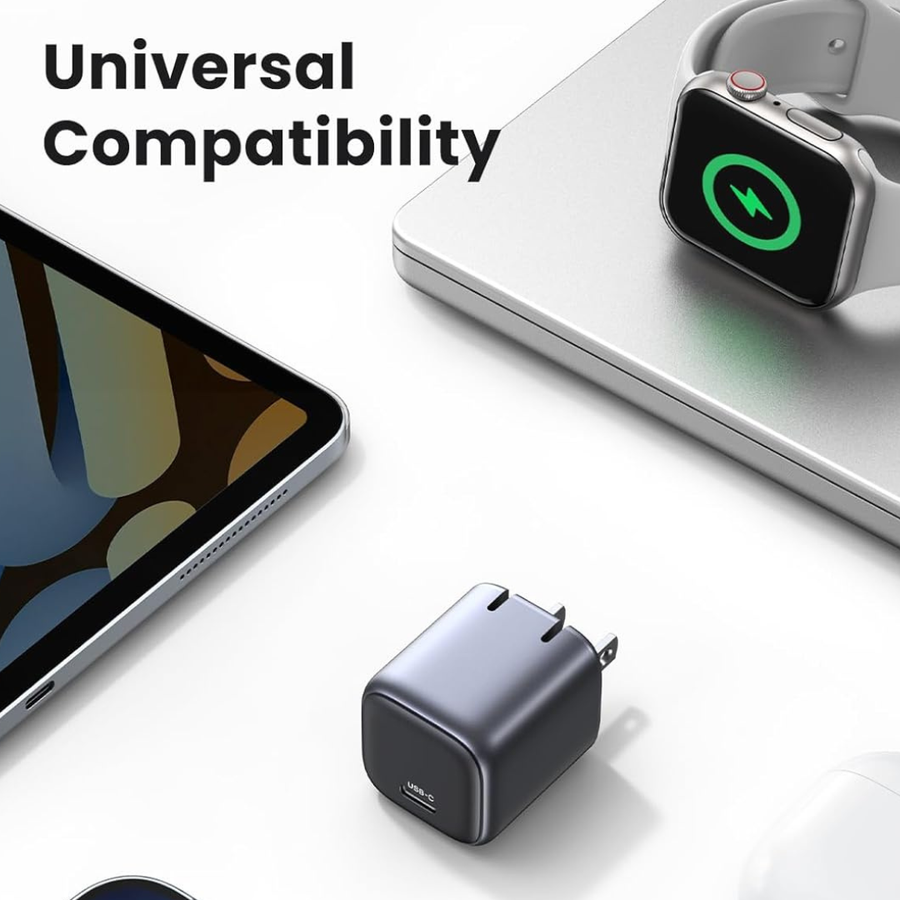 A compact dark gray USB-C wall charger shown on a white surface with a tablet, a smartwatch charging on a laptop, and large text reading 'Universal Compatibility'.