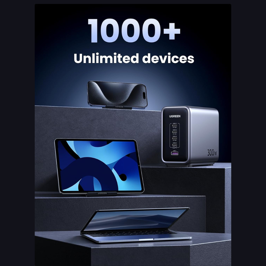 A promotional product render showing a portable power station with a smartphone and tablet plugged in on dark pedestals, with large text reading '1000+ Unlimited devices' above. The power station is branded UGREEN and appears silver and black.