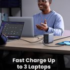 A man sits at a desk using laptops and a tablet, with a dark gray multi-port charger in the foreground. Text at the bottom reads 'Fast Charge Up to 3 Laptops'.
