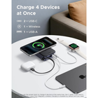 A portable multi-device wireless charging power bank shown on a white round table in a living room setting, charging a smartphone, AirPods, an Apple Watch, and a laptop. The image includes text highlighting its capability to charge 4 devices at once.